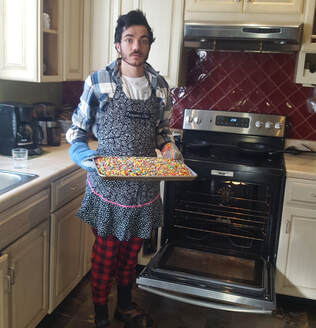Grason holds a pan of colorful items in front of the oven in the L'Arche kitchen